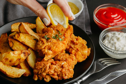 a person dipping a lemon on a plate of fried chicken